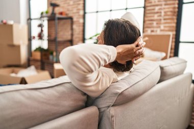 Orta yaşlı bir adam, elleri başının üstünde, yeni evinde kanepede oturuyor.