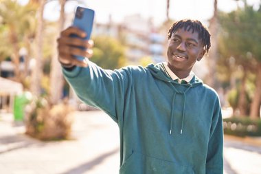 Afro-Amerikalı adam gülümsüyor. Kendine güveni tam. Sokakta akıllı telefondan selfie çekiyor.