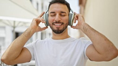 Genç Arap adam sokakta gülümseyen müzik dinliyor.