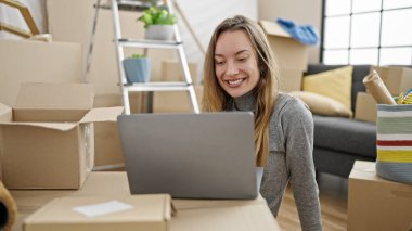 Young caucasian woman using laptop sitting on floor at new home