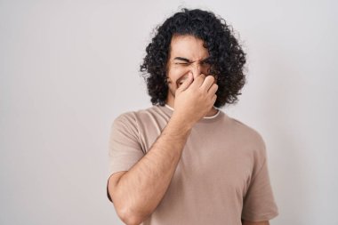 Beyaz arka planda duran kıvırcık saçlı İspanyol bir adam pis ve iğrenç bir koku alıyor. Nefesini burnunda tutuyor. Kötü kokuyor. 