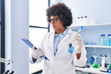 African american woman scientist reading report holding test tube at laboratory