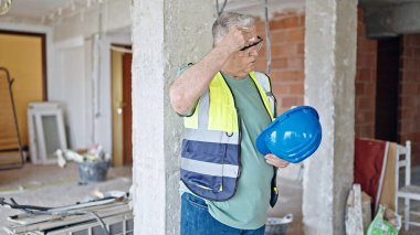 İnşaat alanında terleyen, orta yaşlı, kır saçlı bir inşaatçı.