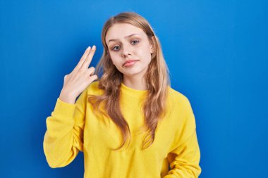 Young caucasian woman standing over blue background shooting and killing oneself pointing hand and fingers to head like gun, suicide gesture. 