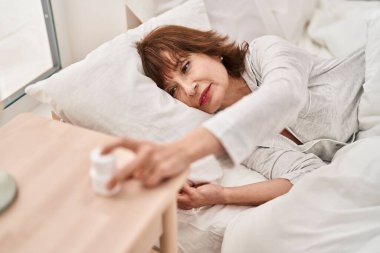 Middle age woman taking pills to sleep lying on bed at bedroom