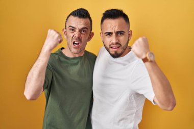 Sarı arka planda dikilen eşcinsel çift kızgın ve kızgın yumruklarını kaldırıyor ve öfkeyle bağırıyor. öfke ve agresif konsept. 