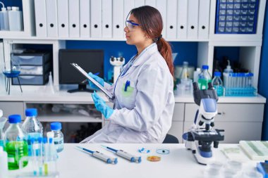 Laboratuvarda çalışan Latin asıllı genç bir kadın. Tarafsız, rahat bir görünüm ve kendine güvenen bir gülümseme arıyor.. 