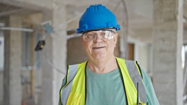 İnşaat alanında kendine gülen, orta yaşlı, gri saçlı bir inşaatçı.