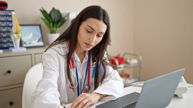 Genç, güzel İspanyol kadın doktor klinikte laptopunu kullanıyor.
