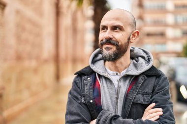 Kel genç adam kollarını kavuşturmuş sokakta el kol hareketi yapıyor.