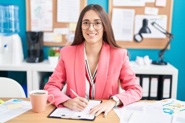 Young hispanic woman working at the office wearing glasses with a happy and cool smile on face. lucky person. 