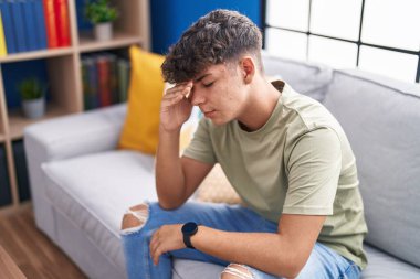 Young hispanic teenager stressed sitting on sofa at home