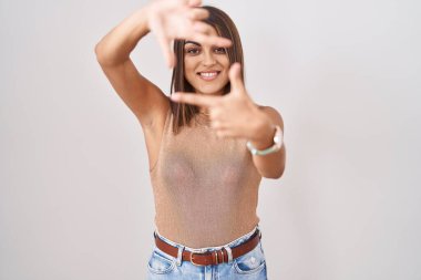 Beyaz arka planda duran genç İspanyol kadın gülümsüyor ve mutlu yüzlü eller ve parmaklarla çerçeve yapıyor. yaratıcılık ve fotoğrafçılık kavramı. 
