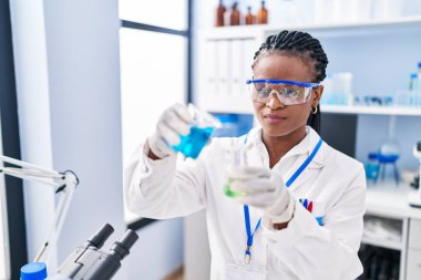 African american woman scientist smiling confident pouring liquid on test tube at laboratory
