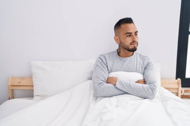 Yatak odasında ciddi bir ifadeyle yatan Latin asıllı genç bir adam.