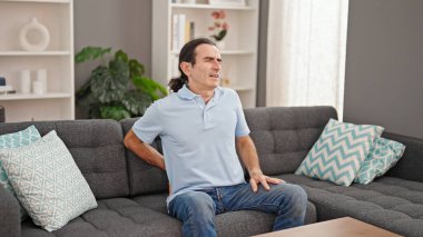 Middle age man suffering for backache sitting on sofa at home
