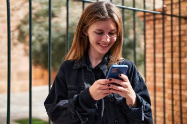 Sokakta gülümseyen akıllı telefon kullanan genç sarışın kadın.
