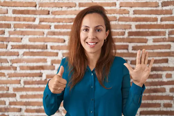 布鲁内特女人站在砖墙上 用六号手指指指点点着 自信而快乐地微笑着 — 图库照片