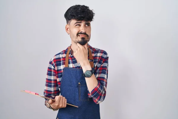 Jovem Hispânico Com Barba Vestindo Avental Garçom Segurando Prancheta Pensando — Fotografia de Stock