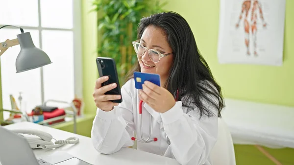 Young chinese woman doctor shopping with smartphone and credit card at the clinic