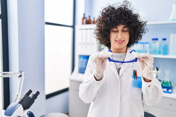 Young middle east woman scientist smiling confident holding security glasses at laboratory
