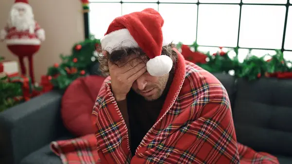 自宅でクリスマスの装飾でソファーに座って毛布で覆う若いヒスパニック男性 — ストック写真
