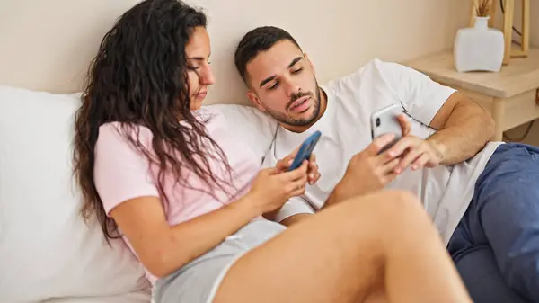 寝室でスマートフォンを使用してベッドに横たわる男女カップル — ストック写真
