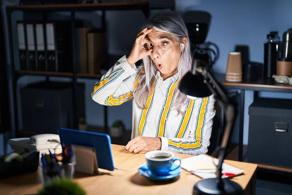 夜にオフィスで働く灰色の髪を持つ中年の女性は 驚いた顔でショックを受け 指を通して見ています 信じられない表現 — ストック写真