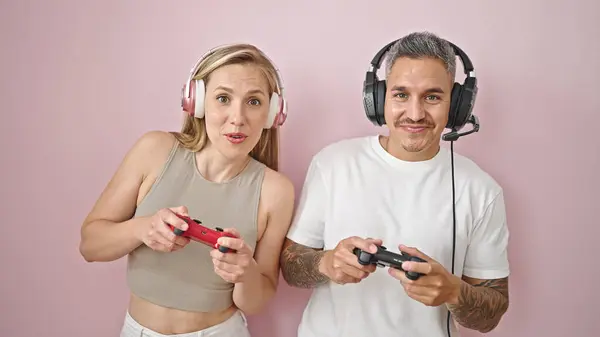 孤立したピンクの背景に微笑むビデオゲームをプレイする男女カップル — ストック写真