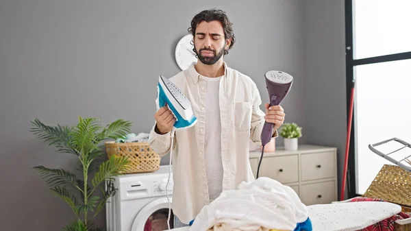 Young hispanic man choosing between ironing machines at laundry room