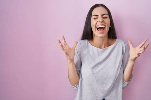 Stock image Young brunette woman standing over pink background celebrating mad and crazy for success with arms raised and closed eyes screaming excited. winner concept 