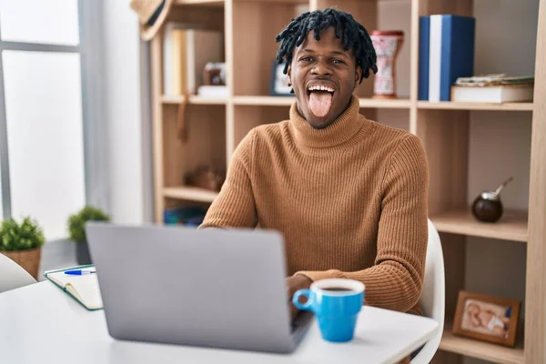 年轻的非洲男人 带着可怕的头发 用电脑笔记本电脑工作 带着滑稽的表情伸出舌头 高兴极了 情感概念 — 图库照片