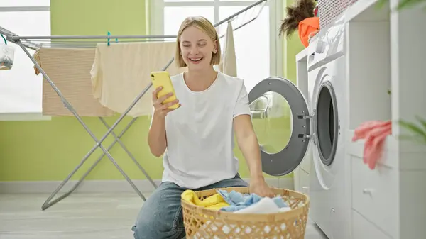Mladá Blondýna Žena Pomocí Smartphone Mytí Oblečení Úsměvem Prádelně — Stock fotografie