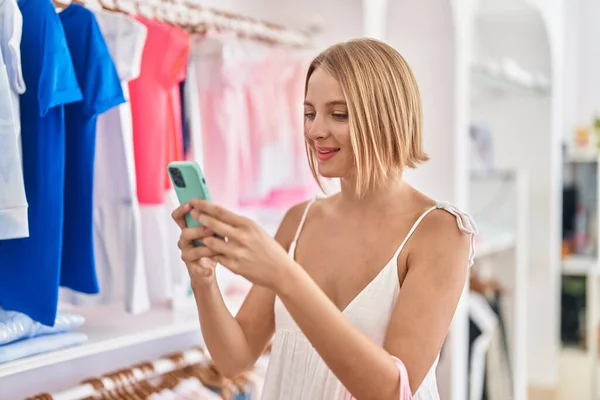 Young blonde woman customer smiling confident using smartphone at clothing store