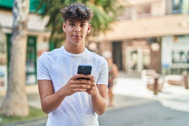 Young hispanic teenager smiling confident using smartphone at street