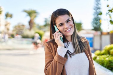 Genç, güzel İspanyol kadın gülümsüyor. Parktaki akıllı telefondan konuşuyor.