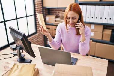 Kafkasyalı genç kadın ecommerce işçisi ofiste akıllı telefon paketinden konuşuyor.