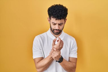 Arap adam sarı arka planda duruyor. Ellerinde ve parmaklarında ağrı var. Eklem iltihabı. 