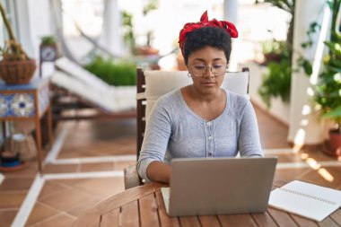 Ev terasındaki masada dizüstü bilgisayar kullanan Afrikalı Amerikalı kadın.