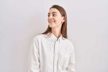 Young caucasian woman standing over isolated background looking away to side with smile on face, natural expression. laughing confident. 