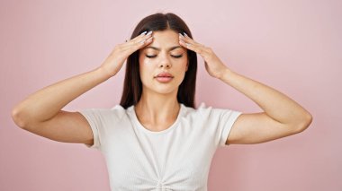 İzole edilmiş pembe arka plan yüzünden baş ağrısı çeken beyaz bir kadın.