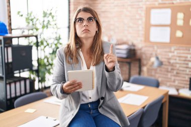 Ofiste çalışan genç İspanyol kadın gözlüklü üzgün ve üzgün görünüyor, parmaklarıyla yönü gösteriyor, mutsuz ve depresif.. 