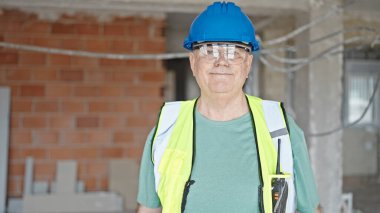 İnşaat alanında kendine gülen, orta yaşlı, gri saçlı bir inşaatçı.