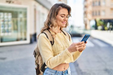 Young woman tourist smiling confident using smartphone at street