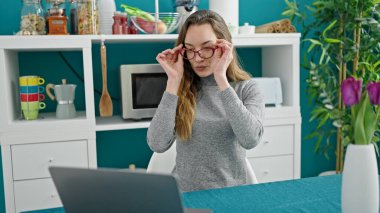 Genç beyaz kadın yemek odasında masada dizüstü bilgisayar kullanıyor.