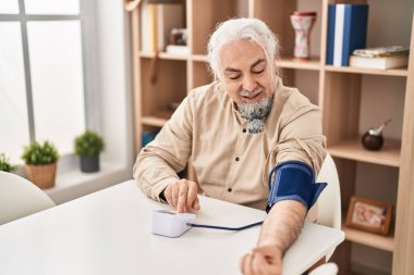 Orta yaşlı, kır saçlı, nabız ölçer kullanan bir adam.