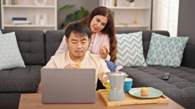 Kadın ve erkek kahvaltıyı evde dizüstü bilgisayarla yapıyorlar.