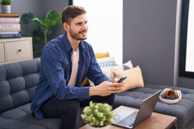Young caucasian man using smartphone and laptop at home