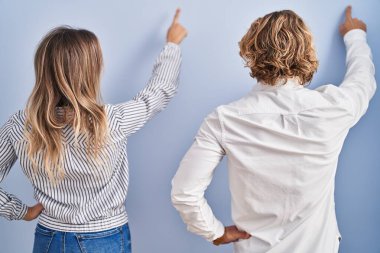 Mavi arka planda duran genç çift, geriye doğru parmak ile ileri doğru poz veriyor. 