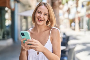 Sokakta akıllı telefon kullanan, kendine güvenen genç sarışın kadın.